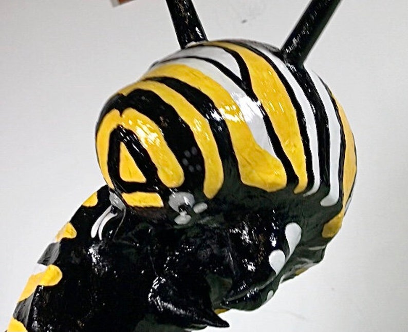 May include: Close-up of a black and yellow striped ceramic sculpture of a caterpillar. The caterpillar has a white stripe on its head and black antennae.