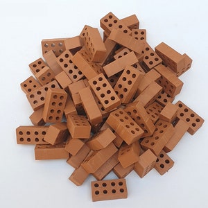 May include: A pile of approximately 30 small, brown, clay bricks with holes. The bricks are arranged in a random pattern.