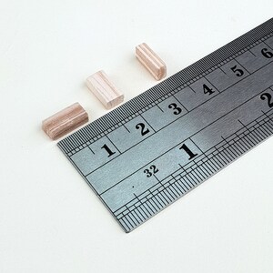 Może przedstawiać: Trzy drewniane klocki o r&oacute;żnych rozmiarach umieszczono na metalowej linijce. Linijka jest oznaczona liczbami od 1 do 6. Klocki są wykonane z tego samego rodzaju drewna, kt&oacute;re ma jasnobrązowy kolor.