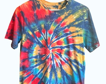 May include: A short-sleeved t-shirt with a vibrant tie-dye pattern. The shirt features a spiral design with a blend of red, blue, yellow, and orange hues. The shirt is hanging on a white hanger against a white background.