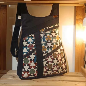 Può includere: Borsa a tracolla nera con un motivo geometrico a triangoli multicolore. Presenta diverse tasche con cerniera e una tracolla regolabile. Una piccola etichetta in pelle è attaccata in alto.