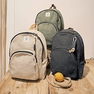 Può includere: Tre zaini diversi realizzati con materiali naturali. Lo zaino a sinistra è beige con una trama tessuta. Lo zaino al centro è verde con una trama tessuta. Lo zaino a destra è nero con una trama tessuta.