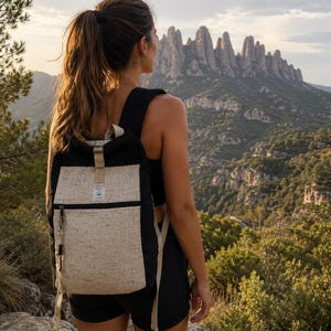 Può includere: Uno zaino nero e beige caratterizzato da una tasca frontale rettangolare con chiusura a zip, un cinturino verticale beige centrale e una piccola etichetta rettangolare bianca con testo nero al centro della parte superiore.