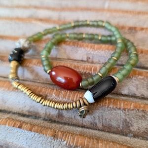 Könnte beinhalten: Eine handgefertigte Halskette mit einer Mischung aus Perlen. Die Halskette enthält olivgrüne, goldene, schwarze und rote Perlen. Das Design integriert eine Vielzahl von Formen und Texturen und schafft so ein einzigartiges Accessoire.