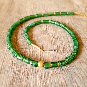 以下が含まれることがあります： 金色のアクセントと「ambra」と書かれた銀色のタグが付いた緑色のガラスビーズネックレスです。