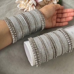 May include: A set of silver bangles with sparkling rhinestones. The bangles are stacked on top of each other and are decorated with intricate designs.