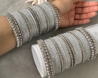 May include: A set of silver bangles with sparkling rhinestones. The bangles are stacked on top of each other and are decorated with intricate designs.