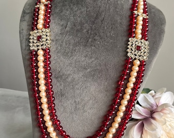 May include: A multi-strand necklace with red and cream glass beads and gold-toned square accents.