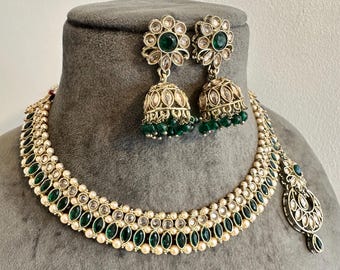 Könnte beinhalten: Ein goldfarbenes Halsketten- und Jhumka-Ohrring-Set mit smaragdgrünen Steinen und kleinen weißen Perlen. Die Halskette hat ein mehrschichtiges Design mit marquise-geschliffenen grünen Steinen und runden Perlen, ergänzt durch blumenförmige Ohrstecker.