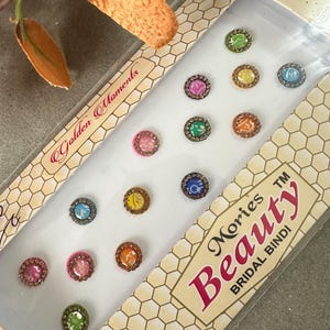 May include: A box of colorful round bindi stickers with the text "Morries Beauty Bridal Bindi" on the front. The box has a honeycomb pattern and the text "Golden Moments" on the side.