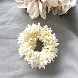 May include: A white flower hair wreath made of fabric flowers. The wreath is in the shape of a circle and is made of many small white flowers.