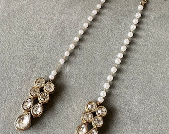May include: A pair of long, gold earrings with a pearl chain and a teardrop-shaped crystal cluster with a green stone at the bottom.