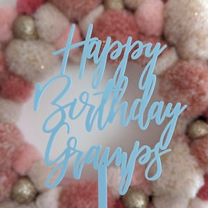 Può includere: Un topper per torta in acrilico blu chiaro con il testo "Happy Birthday Gramps" in corsivo. Il topper è davanti a una ghirlanda di pompon rosa e bianchi.