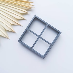 Pode incluir: Um organizador quadrado cinza de quatro seções com um padrão de grade. O organizador é feito de um material liso, semelhante ao plástico.