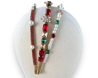 May include: Three gold headbands with red and green jewels and white pearls. The headbands are displayed on a white mannequin head.