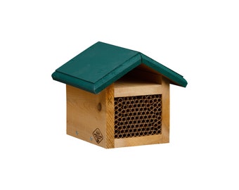 May include: A wooden bee house with a green roof. The house is rectangular with a series of small tubes for bees to nest in. The wood is light brown, and the roof is a dark green. A small logo is visible on the side.