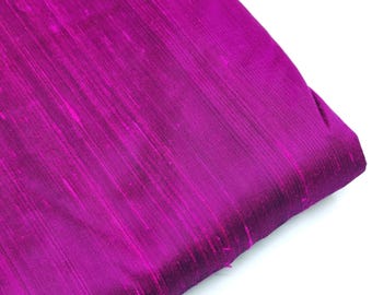 May include: A close-up of a vibrant magenta silk fabric with a subtle sheen. The fabric has a smooth, flowing texture and is folded in a triangular shape.