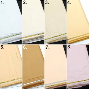 May include: A collection of eight folded fabric bolts in various shades including white, cream, beige, tan, and light pink. Each bolt features a decorative yellow and black trim along the bottom edge with the text 100% PREMIUM GIZA COTTON.