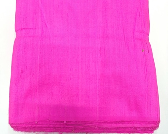 May include: A folded stack of bright pink fabric. The material has a textured appearance with vertical lines and a slightly uneven surface. The edges of the fabric are frayed, suggesting a raw or unfinished state. The color is a vibrant, saturated pink.