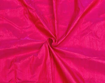 May include: A close-up of a bright pink fabric with a smooth, silky texture. The fabric is folded and draped, creating soft folds and wrinkles.