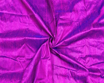 May include: A close-up of a vibrant purple fabric with a subtle iridescent sheen. The fabric is folded and draped, showcasing its soft texture and flowing lines.