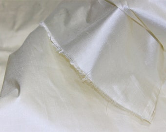 May include: A close-up of a piece of ivory white silk fabric with a raw edge. The fabric is smooth and has a slight sheen.