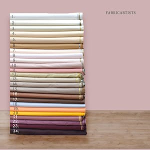 May include: A stack of twenty-four folded fabric bolts arranged vertically, labeled with numbers one through twenty-four. The collection features a gradient of solid colors ranging from white and cream to beige, pink, blue, yellow, and dark brown.