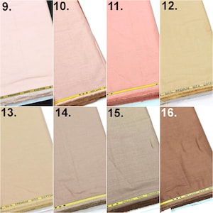 May include: A collection of eight fabric swatches in various shades of pink, beige, and brown. Each piece of fabric features a yellow selvage edge with the printed text 100% PREMIUM GIZA COTTON. The textiles display a fine, woven texture.