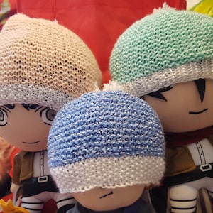 May include: Three knitted hats in different colors: light pink, light blue, and light green. Each hat has a white band at the bottom. The hats are worn by three plush toys.