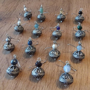 Könnte beinhalten: Eine Sammlung handgefertigter Silberohrringe, jeweils mit einem filigranen Kugeldesign und einem Edelstein- oder Perlenakzent. Die Ohrringe haben ein einzigartiges, skurriles Aussehen, mit kleinen Drahtarmen, die von der Kugel ausgehen.