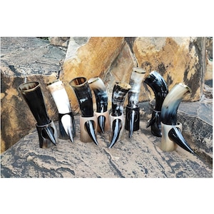 Może przedstawiać: Kolekcja ośmiu rogów do picia, każdy z metalową obręczą i podstawą. Rogi są wykonane z naturalnych materiałów i mają różne kolory i wzory.