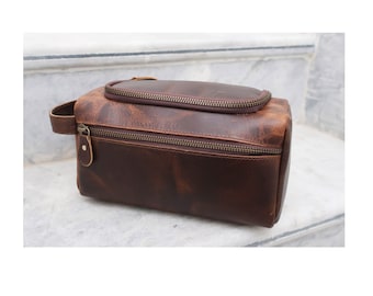 May include: A brown leather travel toiletry bag with two zippered compartments. The bag has a top handle and a distressed leather finish.