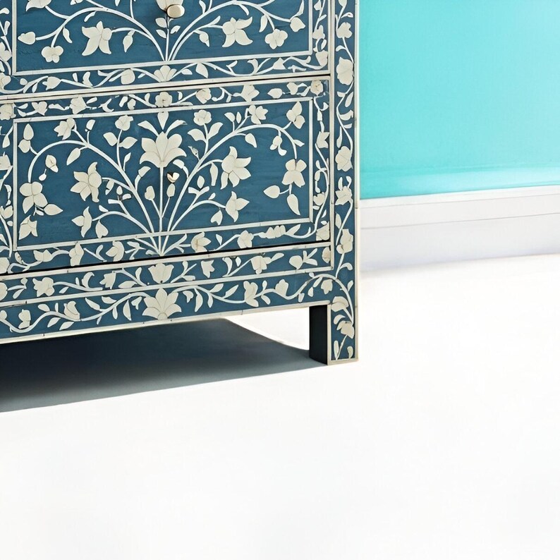 Puede incluir: Un aparador azul con intrincados dise&ntilde;os florales blancos. El aparador tiene cuatro cajones y se apoya en cuatro patas cortas.