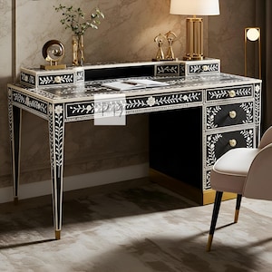 以下が含まれることがあります： 真珠貝でできた複雑な花の象嵌細工が施された黒い机。机は背もたれが高く、右側に3つの引き出しがあります。机は金色のアクセントで飾られており、白い大理石の天板があります。