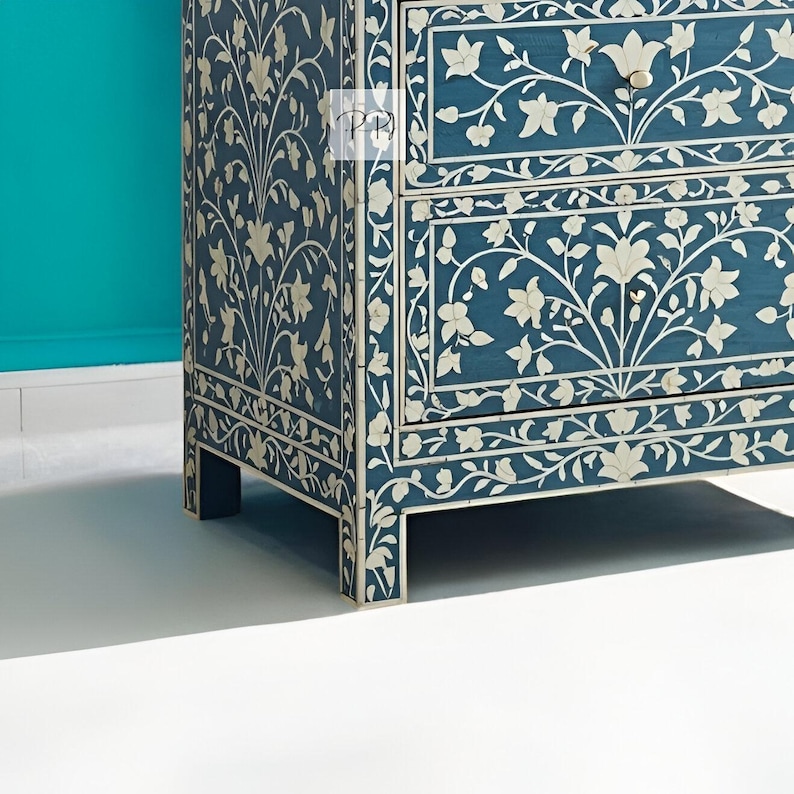 Puede incluir: Un cofre de cajones azul con incrustaciones florales blancas. El cofre tiene dos cajones y se apoya en cuatro patas.