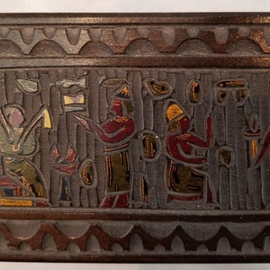 May include: A wooden box with a carved design of people in colorful clothing. The box is decorated with a geometric pattern around the edge.