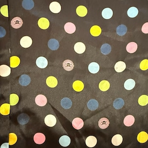 May include: Black fabric with a polka dot pattern in various colors, including yellow, pink, blue, and white. The fabric also features a repeating circular logo design. The overall design is playful and colorful.
