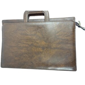 May include: A rectangular brown briefcase with a distressed, mottled texture. The bag features a structured top handle integrated into the frame and a side zipper closure with a metallic pull tab. The surface displays varied dark and light brown tones.