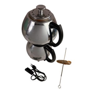 May include: A chrome electric coffee maker with black handles and a lid. A metal skewer with a small, round, brown object is next to the coffee maker. A black power cord is also included.