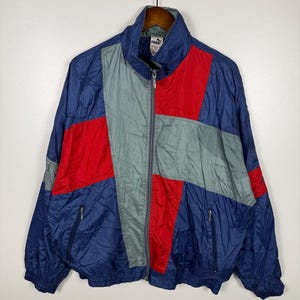 Pode incluir: Casaco de treino Puma vintage em azul marinho, vermelho e cinza. O casaco tem fecho de correr completo, dois bolsos frontais e gola alta. O design em blocos de cores é um estilo retro clássico.