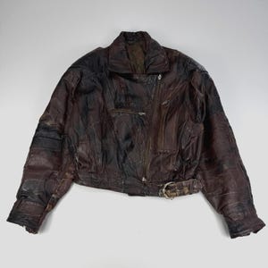 Peut inclure: Une veste en cuir marron foncé présentant un motif en patchwork avec de multiples empiècements, une fermeture éclair frontale diagonale, un large col, des manches longues avec poignets zippés et une ceinture ajustable à boucle métallique.