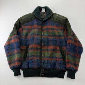 May include: A long-sleeve bomber jacket featuring a fuzzy, multi-colored plaid pattern in shades of blue, green, and orange. The jacket includes dark green suede shoulder panels, a ribbed knit collar, cuffs, and hem, and a front button closure.