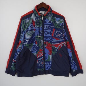 May include: A vintage zip-up jacket with a colorful abstract pattern in blue, green, and red. The jacket has a navy blue base with red stripes on the sleeves and a navy blue collar. It features two front pockets and a full zipper.