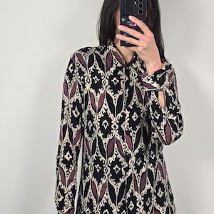 May include: A long-sleeved button-down shirt with a black, cream, and burgundy geometric pattern. The shirt has a collared neckline and buttoned cuffs. The pattern is a repeating design of stylized shapes.