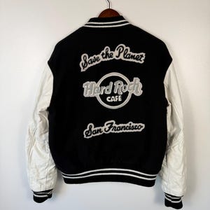 May include: A white ceramic mug with a black handle and the text "But First, Coffee" in a bold, black font. The mug is set against a blurred background, suggesting a cozy setting.