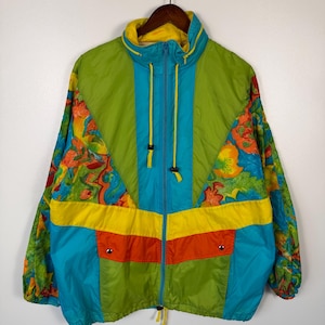 May include: A vintage, color-blocked jacket with a vibrant design. The jacket features a combination of green, blue, yellow, and orange panels. Floral patterns adorn the sleeves. It has a zip-up front, a high collar, and drawstrings.