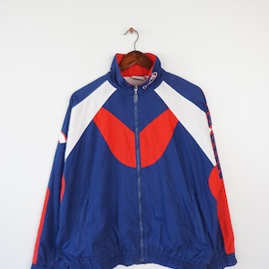 May include: A blue, red, and white windbreaker jacket with a zipper closure. The jacket has a stand-up collar and a white logo on the right sleeve.