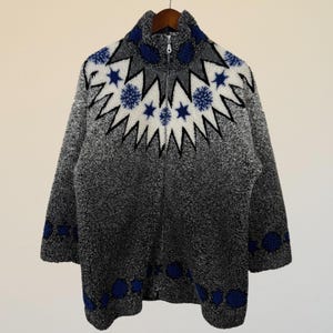 May include: A gray fleece jacket with a full zipper and a unique geometric pattern. The pattern features white starbursts and blue floral accents around the collar and cuffs. The jacket is hanging on a wooden hanger.