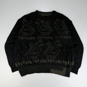 Könnte beinhalten: Ein schwarzer Langarmpullover mit Rundhalsausschnitt und einem sich wiederholenden geometrischen Muster aus stilisierten vogelartigen Figuren in einem gedämpften Olivgrün. Das Strickkleidungsstück hat gerippte Bündchen an Kragen, Ärmeln und Saum.