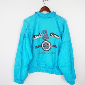 May include: A turquoise blue windbreaker jacket with a white, purple, and gray "Uncle A Sam" logo on the back. The logo includes the text "True Mark Fashion Line" and "The Trademark of Allwear".